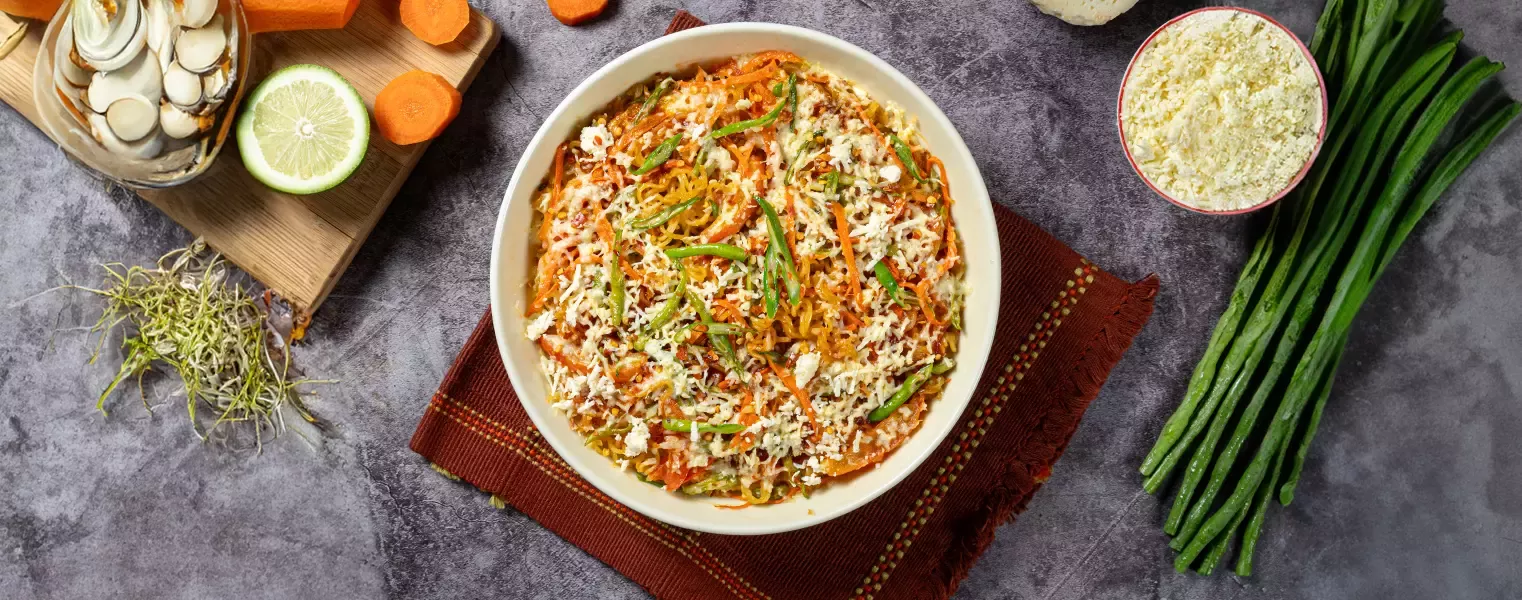 Baked cheesy noodles with maggi topped with vegetables and melted cheese in bowl