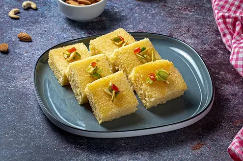 A plate of yellow-colored sweet dessert pieces garnished with nuts, displayed on a dark background