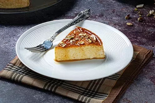 A slice of cheesecake placed on a white plate with nuts sprinkled on top, beside a fork.