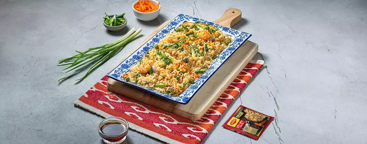 Chicken and vegetable fried rice with maggi seasoning served on platter with garnishes