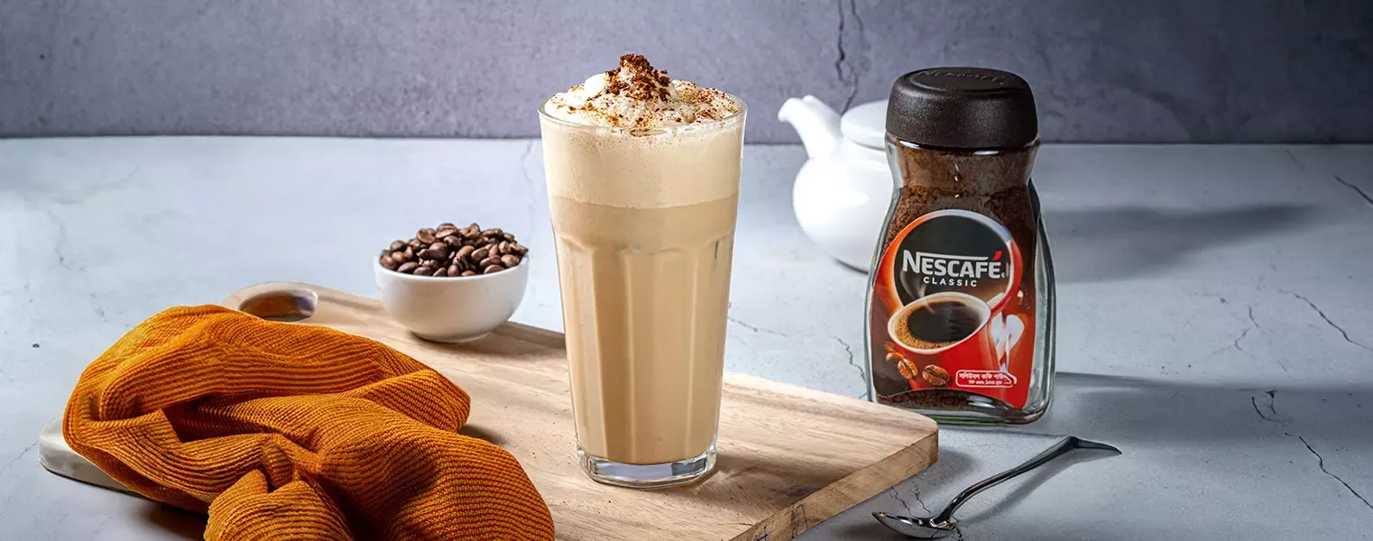 Chilled butterscotch coffee with nescafe topped with foam served in tall glass