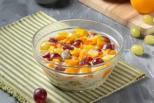 A fruit salad in a glass bowl with a variety of fresh fruits, including grapes and mangoes, arranged on a striped mat.